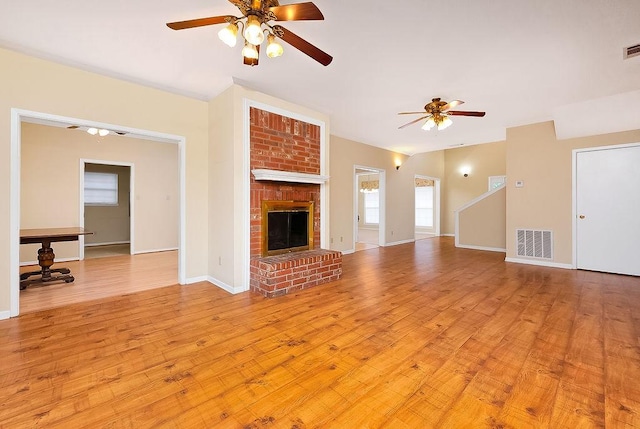 unfurnished living room featuring ceiling fan, a fireplace, visible vents, baseboards, and light wood-style floors