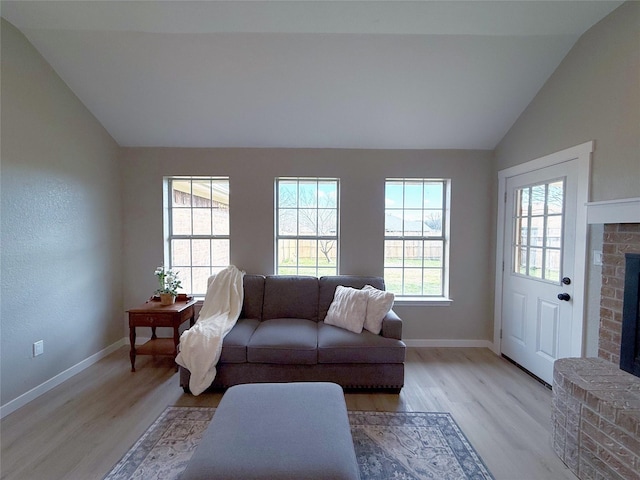 living room featuring lofted ceiling, a fireplace, light wood-style flooring, and baseboards