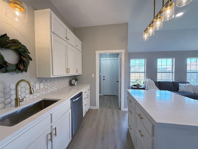 kitchen with light wood-style flooring, backsplash, open floor plan, stainless steel dishwasher, and a sink