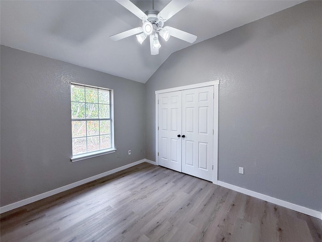 unfurnished bedroom with baseboards, ceiling fan, wood finished floors, vaulted ceiling, and a closet