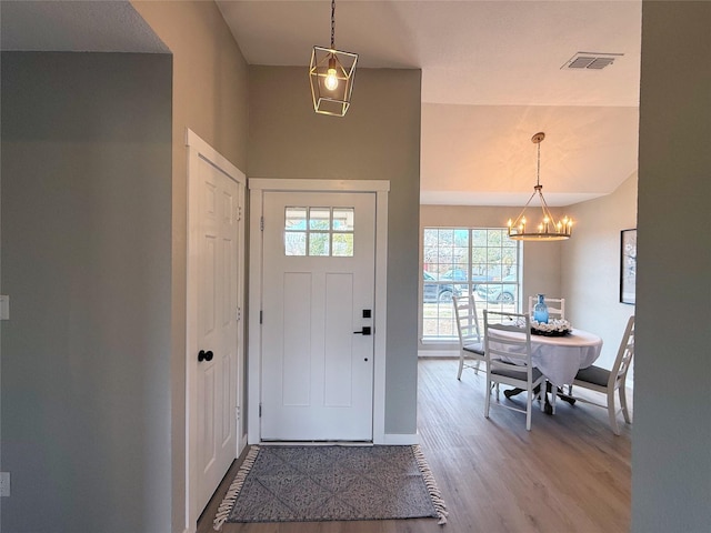 foyer featuring visible vents, a notable chandelier, baseboards, and wood finished floors