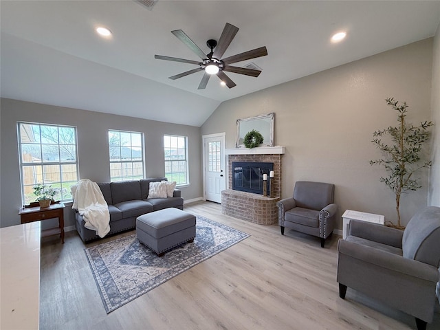 living area featuring baseboards, a ceiling fan, vaulted ceiling, light wood-type flooring, and a fireplace