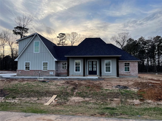 view of front of home featuring brick siding, board and batten siding, and a shingled roof