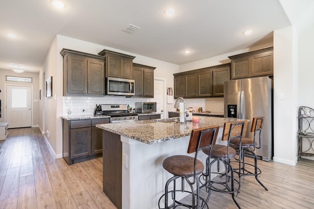 kitchen featuring dark brown cabinetry, visible vents, appliances with stainless steel finishes, light stone countertops, and a sink