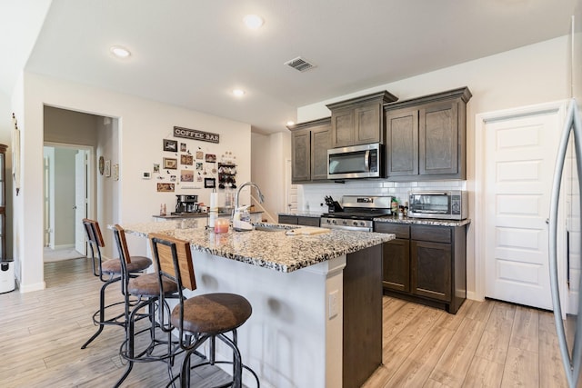 kitchen featuring visible vents, appliances with stainless steel finishes, light stone counters, a kitchen bar, and a sink