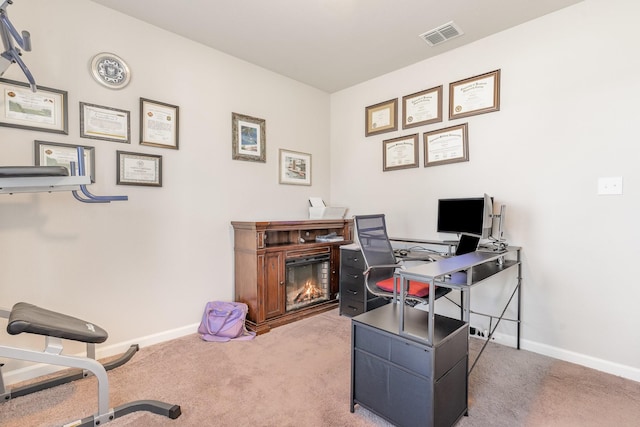 carpeted office featuring a glass covered fireplace, visible vents, and baseboards