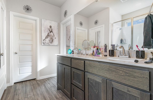 bathroom featuring wood finished floors, a sink, baseboards, a shower stall, and double vanity