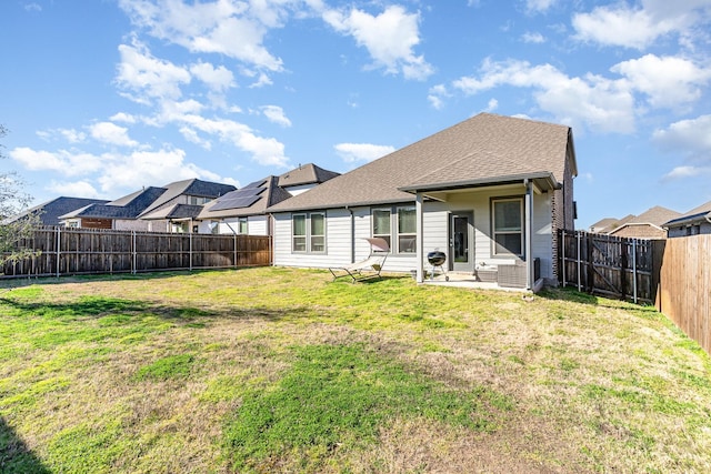 back of house featuring a fenced backyard, a shingled roof, a lawn, and a patio