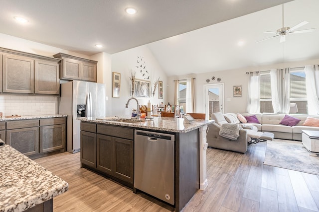 kitchen featuring a center island with sink, appliances with stainless steel finishes, vaulted ceiling, light wood-type flooring, and a sink