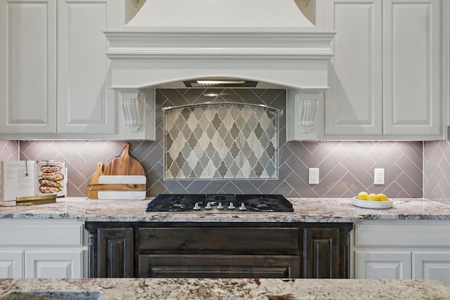 kitchen featuring stainless steel gas cooktop, decorative backsplash, white cabinetry, and light stone countertops