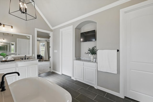 bathroom with lofted ceiling, a soaking tub, a sink, crown molding, and two vanities