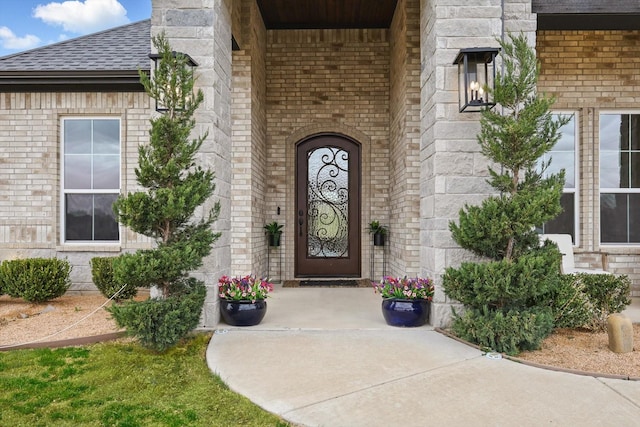 view of exterior entry featuring a shingled roof and brick siding