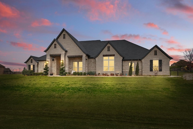 french country home featuring roof with shingles and a yard