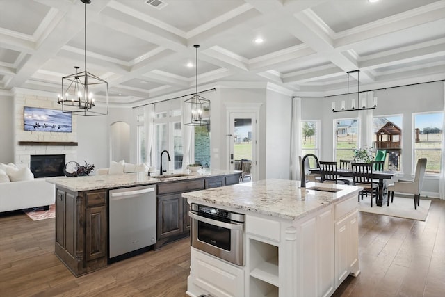 kitchen with stainless steel appliances, a stone fireplace, a sink, and a center island with sink