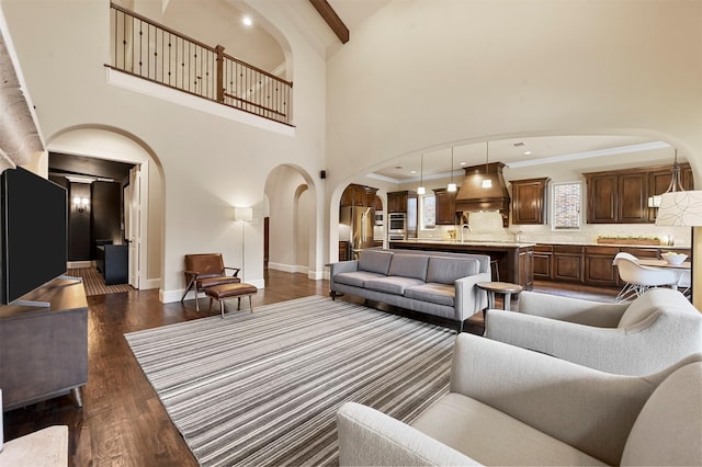 living area with arched walkways, a high ceiling, baseboards, ornamental molding, and dark wood-style floors