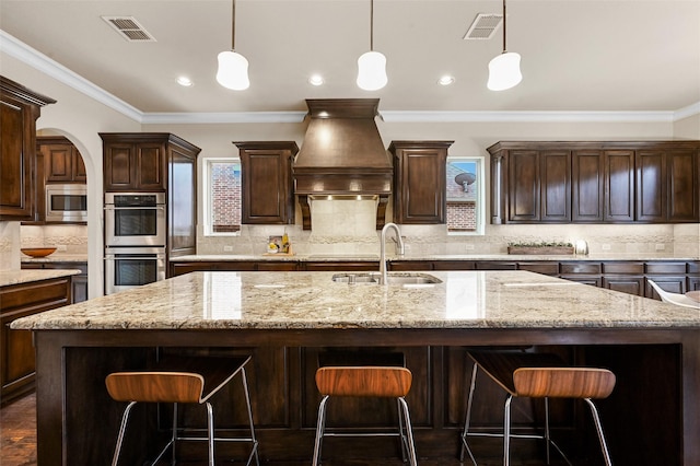 kitchen with visible vents, a kitchen island with sink, custom exhaust hood, stainless steel appliances, and a sink