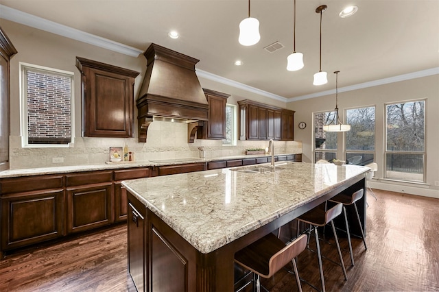 kitchen with dark wood-style flooring, black electric stovetop, custom range hood, visible vents, and a sink