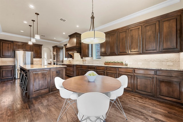 kitchen with appliances with stainless steel finishes, custom range hood, dark brown cabinets, and dark wood-type flooring