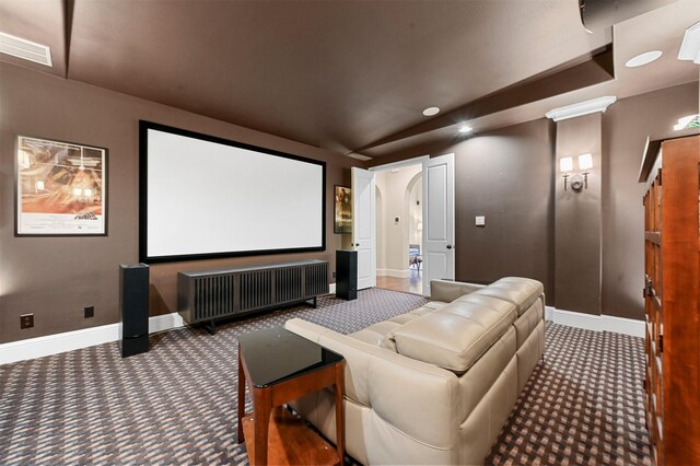 carpeted home theater room with baseboards, visible vents, arched walkways, radiator, and vaulted ceiling