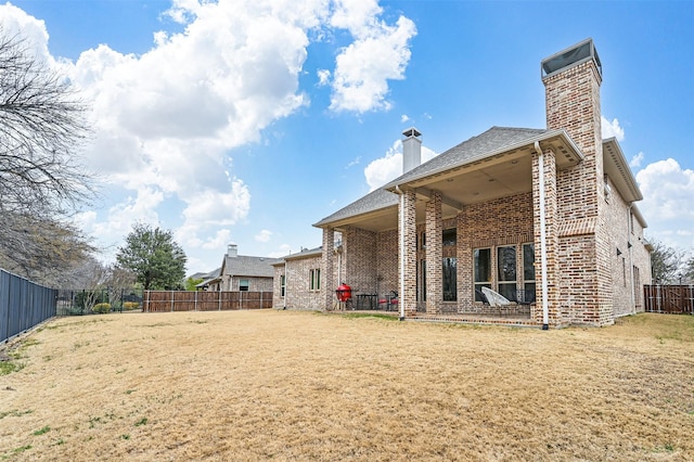 rear view of property featuring brick siding, a lawn, a chimney, and a fenced backyard