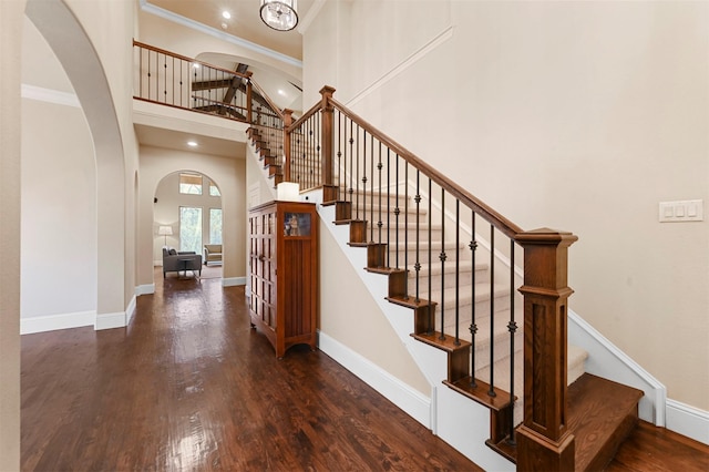 stairway featuring arched walkways, a high ceiling, wood finished floors, and baseboards