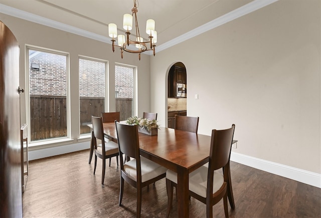 dining area featuring arched walkways, an inviting chandelier, dark wood-type flooring, ornamental molding, and baseboards