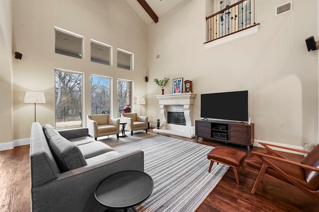 living area featuring wood finished floors, visible vents, baseboards, beam ceiling, and a glass covered fireplace