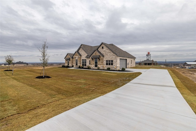 french provincial home featuring a garage, stone siding, driveway, and a front lawn