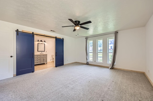 unfurnished bedroom with a textured ceiling, a barn door, visible vents, and light colored carpet