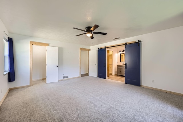 unfurnished bedroom featuring light carpet, a barn door, visible vents, and baseboards