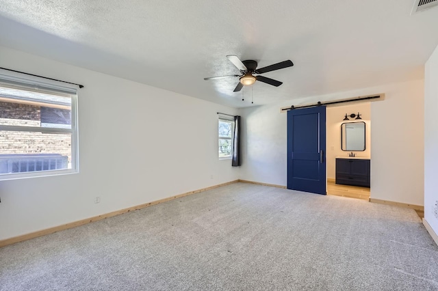 unfurnished bedroom with light colored carpet, visible vents, a barn door, a textured ceiling, and baseboards