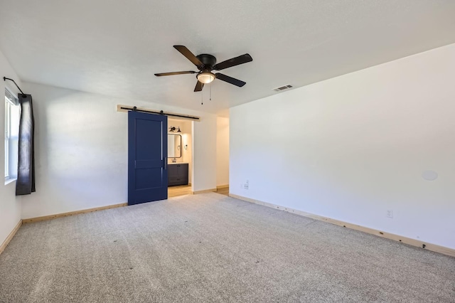 spare room with a barn door, light colored carpet, visible vents, baseboards, and a ceiling fan