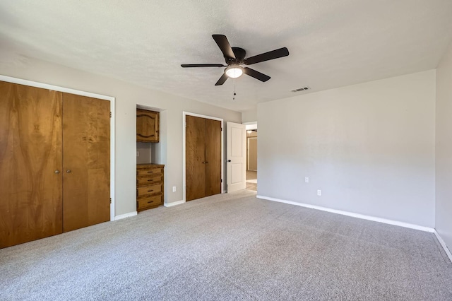 unfurnished bedroom featuring baseboards, carpet floors, visible vents, and multiple closets