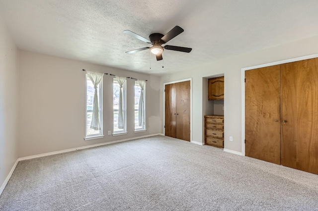 unfurnished bedroom with carpet floors, multiple closets, a ceiling fan, a textured ceiling, and baseboards