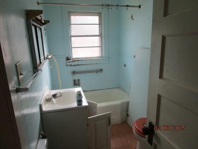 bathroom featuring toilet, wood finished floors, vanity, and a tub