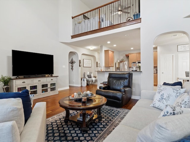 living area with arched walkways, a towering ceiling, baseboards, and wood finished floors