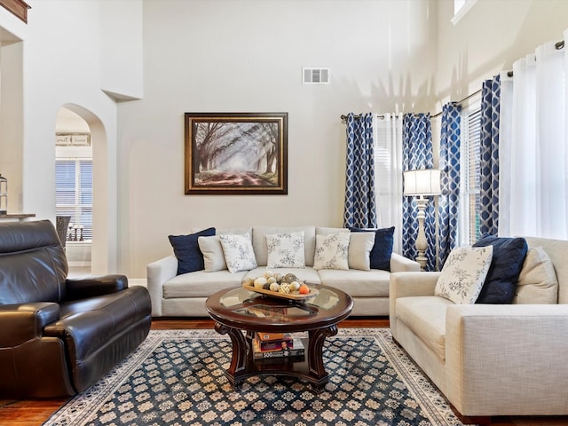 living area with arched walkways, visible vents, a towering ceiling, and wood finished floors