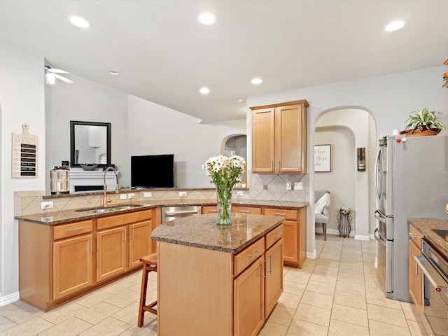 kitchen featuring arched walkways, stainless steel appliances, a peninsula, a sink, and backsplash