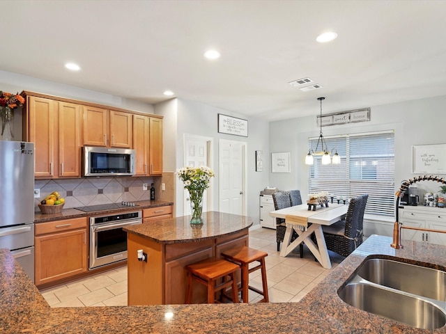 kitchen with dark stone countertops, stainless steel appliances, light tile patterned flooring, and a sink