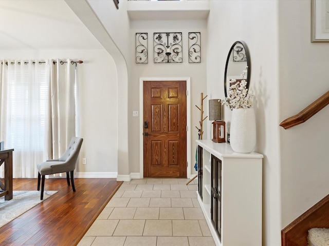 foyer featuring arched walkways, stairway, baseboards, and light tile patterned floors