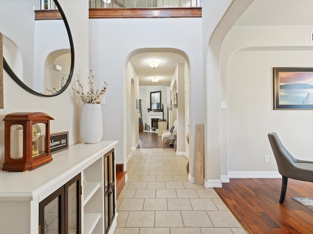 hallway featuring arched walkways, a towering ceiling, baseboards, and light tile patterned floors