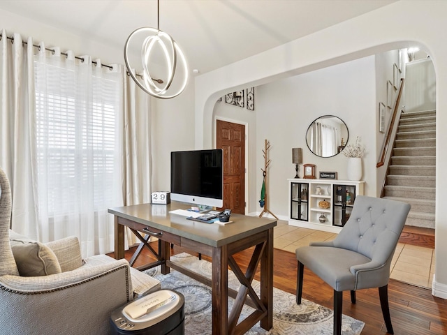 home office featuring arched walkways, a notable chandelier, and wood finished floors