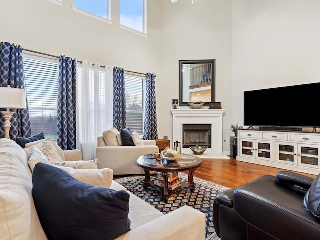 living room featuring a wealth of natural light, a fireplace with raised hearth, a towering ceiling, and wood finished floors