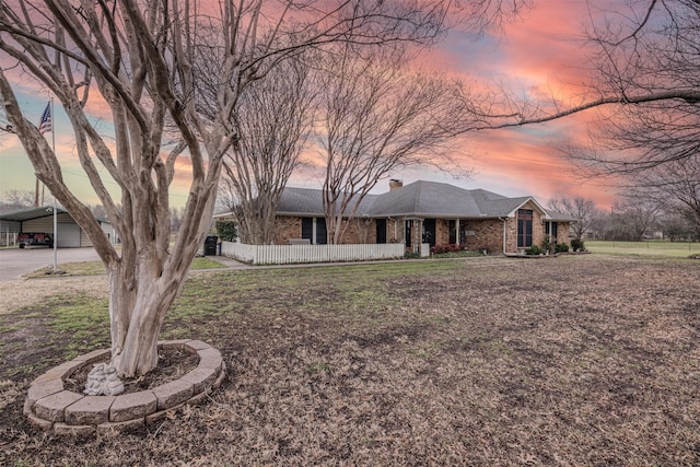 ranch-style home featuring brick siding, a chimney, a shingled roof, a lawn, and fence