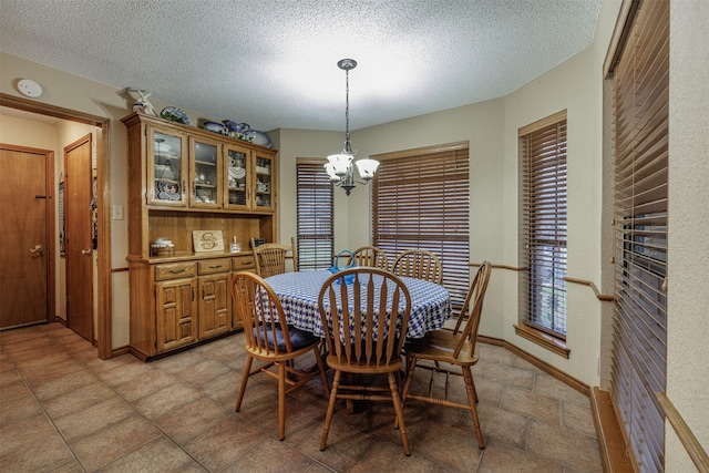 dining room with a textured ceiling, stone finish floor, baseboards, and a notable chandelier