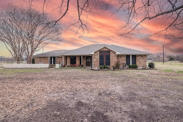 view of front facade with brick siding, roof with shingles, and fence