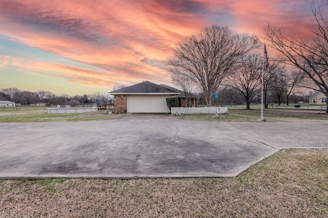 view of property exterior featuring driveway, a garage, a lawn, fence, and brick siding