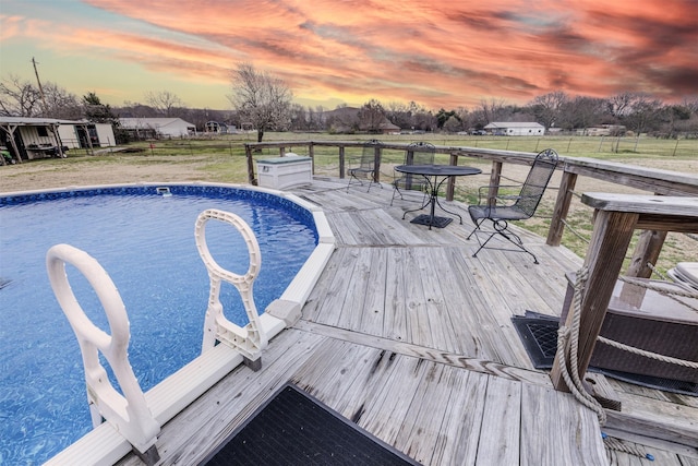 pool at dusk with fence, a wooden deck, and an outdoor pool