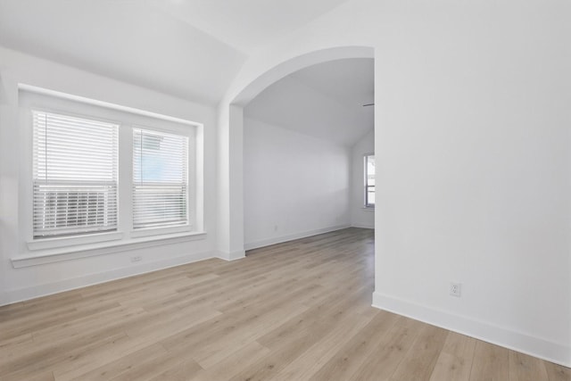 empty room featuring baseboards, lofted ceiling, arched walkways, and light wood-type flooring