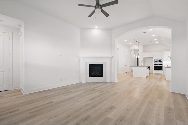 unfurnished living room with light wood finished floors, ceiling fan, recessed lighting, arched walkways, and lofted ceiling